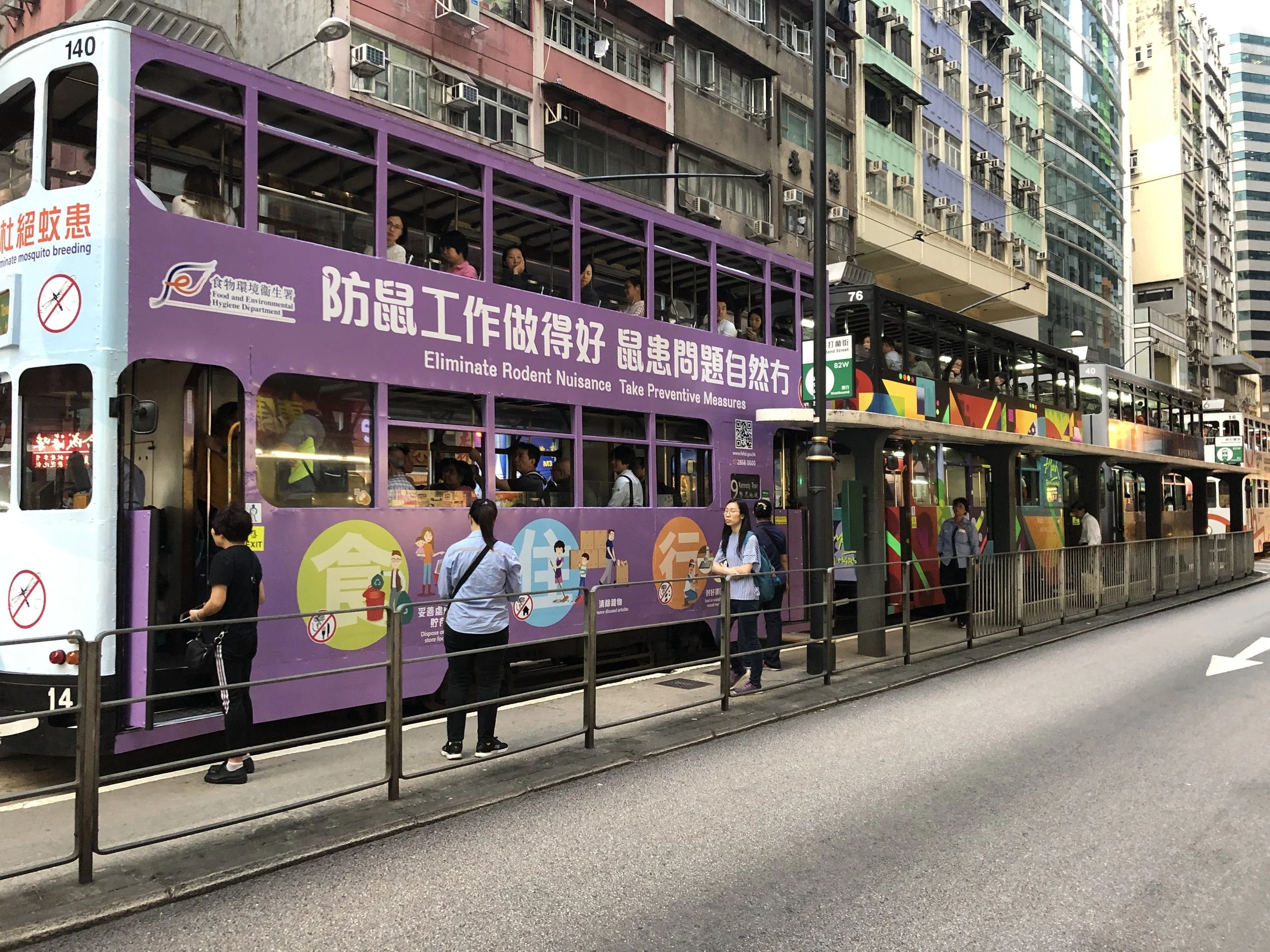 A vintage tram passing shopfronts on a Hong Kong street