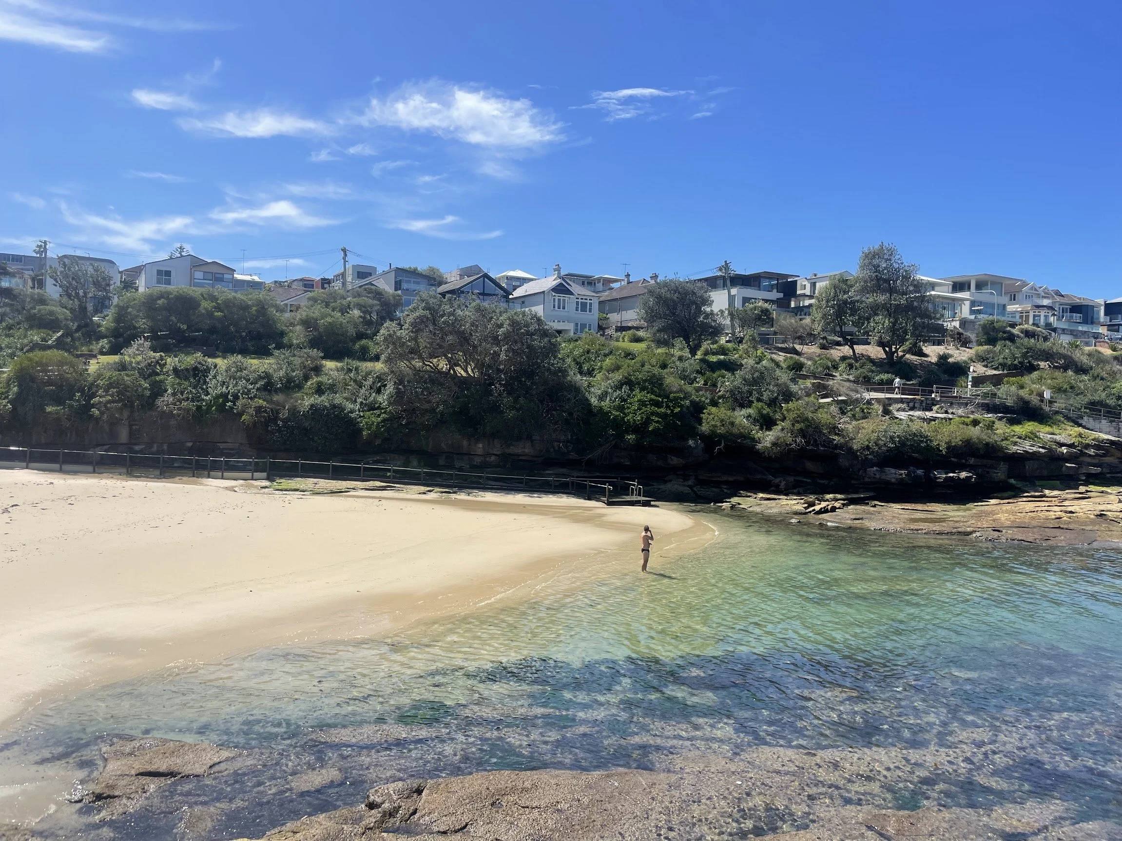 A quiet sandy cove with clear shallow water and hillside homes