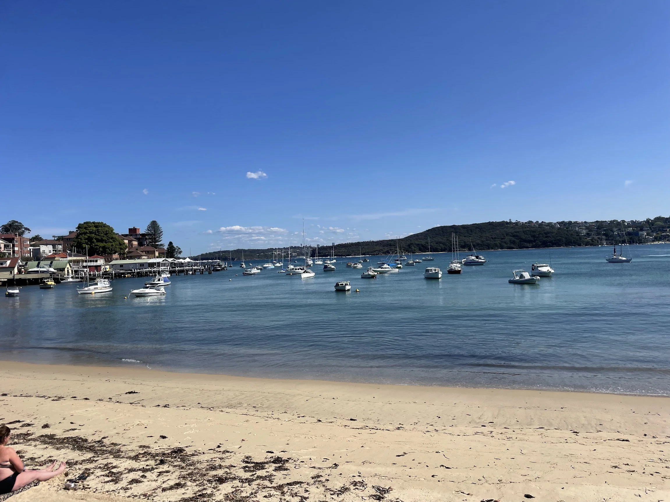 Sailboats moored in a calm harbour bay beside a sandy beach