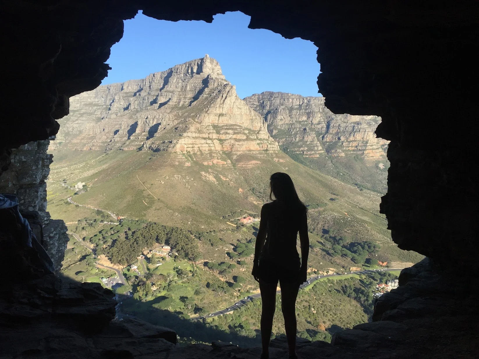 A figure silhouetted in a mountain cave looking out over the valley